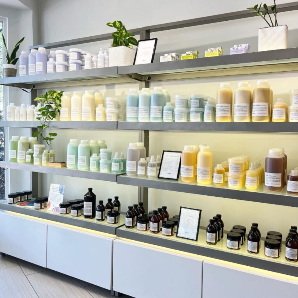 Shelves displaying various bottles of skincare or haircare products in a store, with small plants decorating the area. - Detlev Lifestyle Salon in Coconut Grove, FL