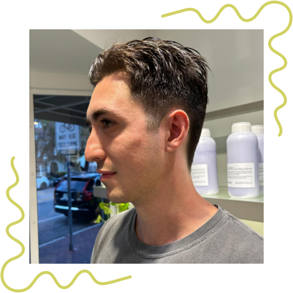 Side profile of a person with short, dark hair in a salon. Shelves with bottles are in the background. - Detlev Lifestyle Salon in Coconut Grove, FL
