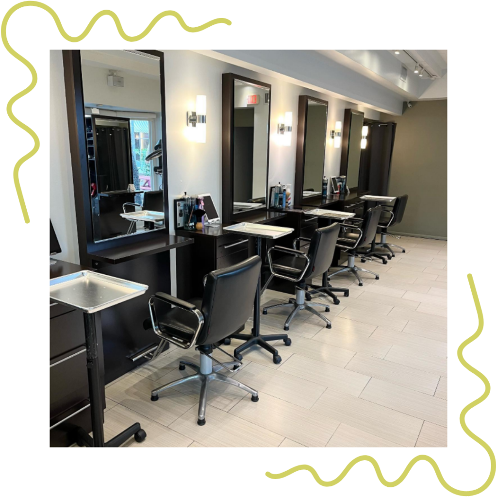 Empty hair salon with four black styling chairs, mirrors, and stations along a wall. The floor is light-colored, and the interior is modern with overhead lighting. - Detlev Lifestyle Salon in Coconut Grove, FL