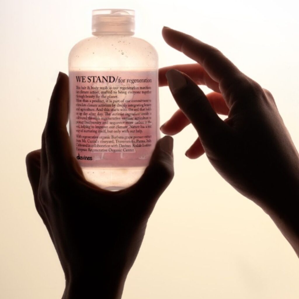 Hands holding a clear bottle with a printed label titled "WE STAND for regeneration" against a soft, light background. - Detlev Lifestyle Salon in Coconut Grove, FL