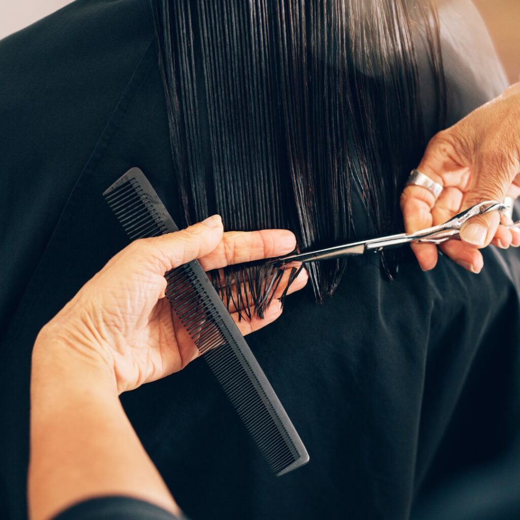 Close-up of a person getting their straight, wet hair trimmed with scissors while another hand holds a black comb—a technique used by top stylists to achieve perfect haircuts. - Detlev Lifestyle Salon in Coconut Grove, FL