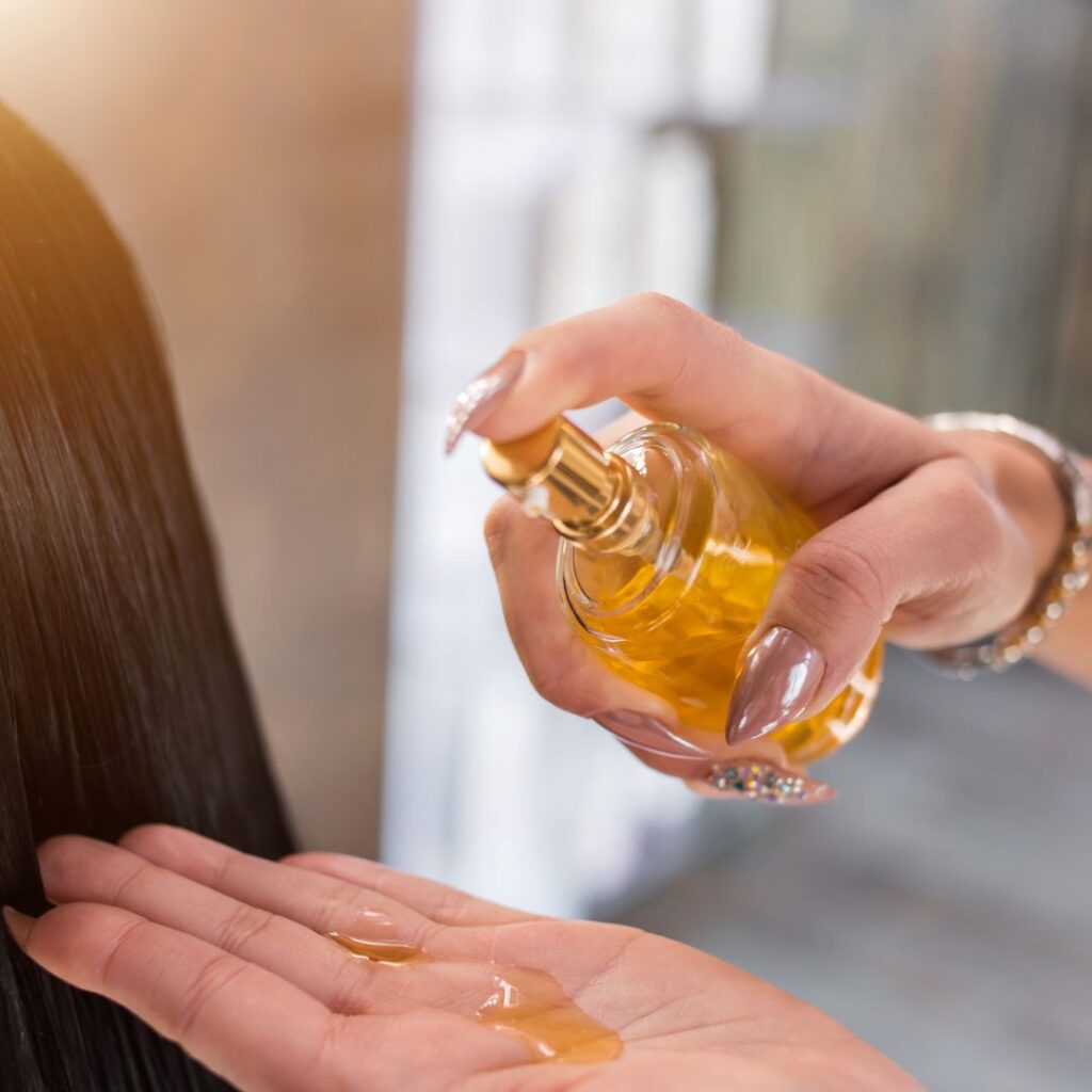 A person spritzes the golden liquid from a clear bottle onto their hand. With manicured nails, they savor the hydration boost perfect for humid climates. The blurred background highlights this serene moment. - Detlev Lifestyle Salon in Coconut Grove, FL