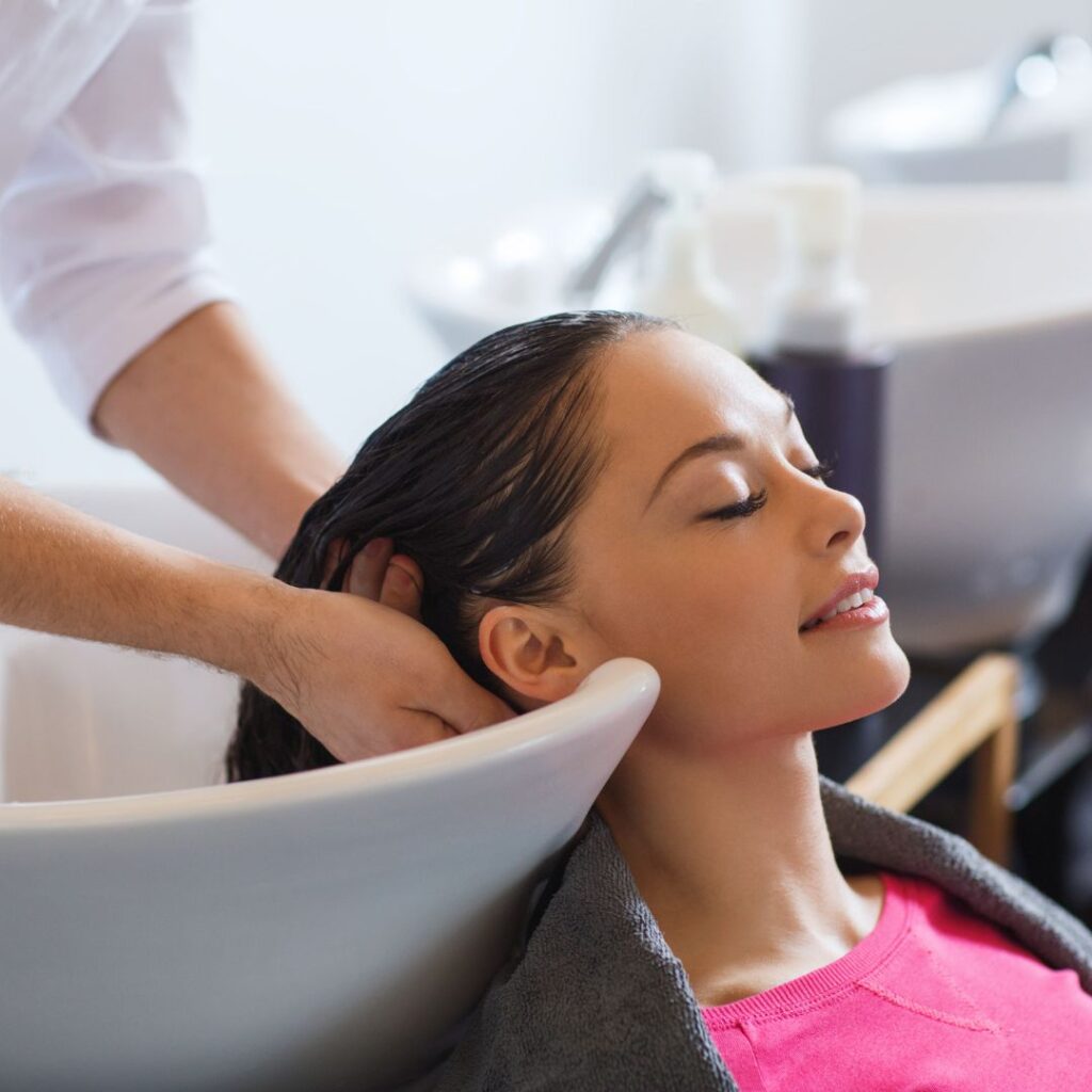 A person with long dark hair enjoys a soothing hair wash in a salon, reclining with eyes closed as the stylist gently rinses their hair at the sink, leaving their locks primed for gorgeous haircuts. - Detlev Lifestyle Salon in Coconut Grove, FL