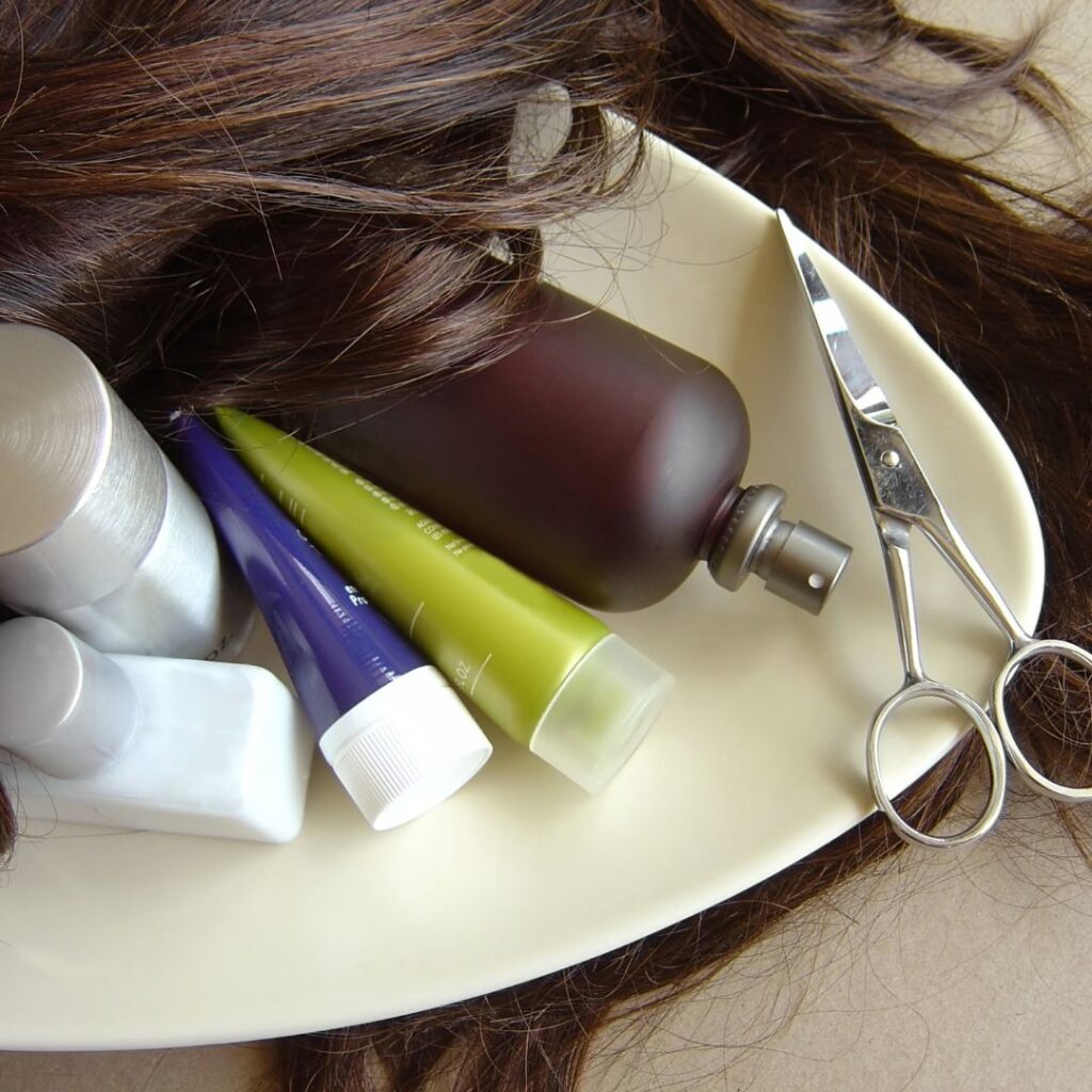 A pair of scissors, luxury hair treatments, and strands of brown hair are artfully arranged on a white oval tray at Detlev Salon. - Detlev Lifestyle Salon in Coconut Grove, FL