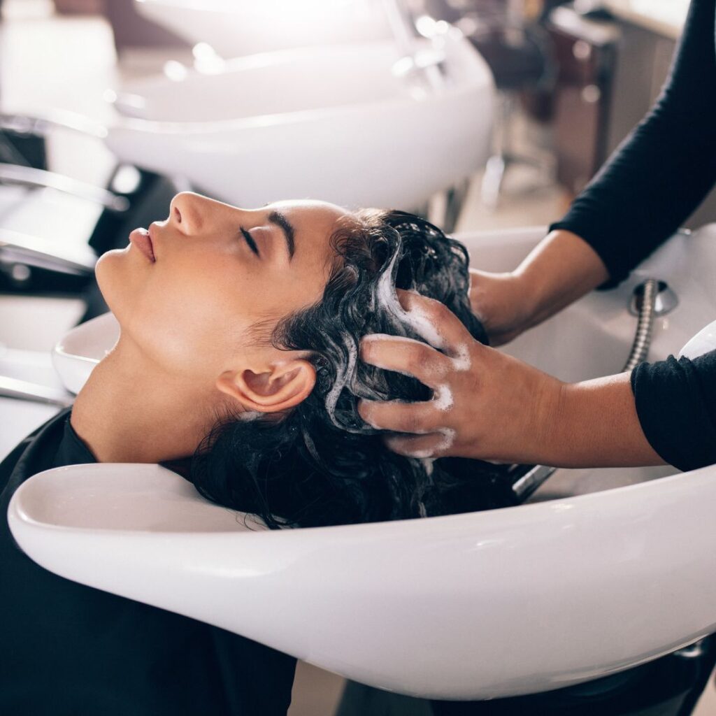 Person getting hair washed at a salon sink by a stylist, with closed eyes and soapy hands massaging their scalp—experience the ultimate relaxation and revitalize your locks with luxury hair treatments. - Detlev Lifestyle Salon in Coconut Grove, FL