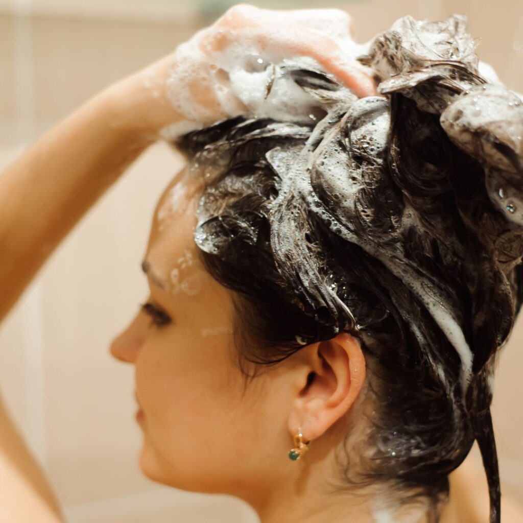 A person is shampooing their hair, covered in foam, with one hand on their head, as they indulge in a revitalizing experience usually reserved for luxury hair treatments. - Detlev Lifestyle Salon in Coconut Grove, FL