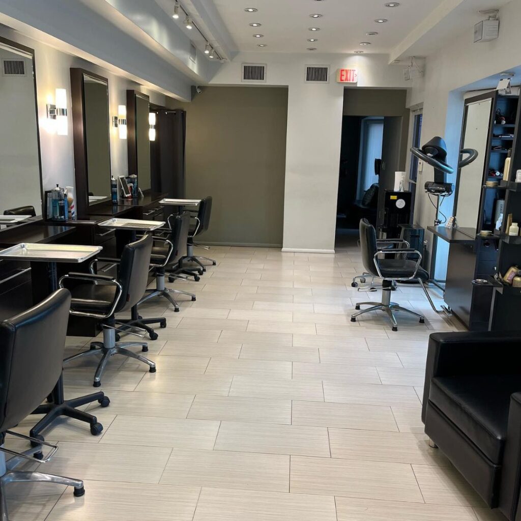 A modern, well-lit hair salon interior offering a unique salon experience with several empty styling stations, black chairs, mirrors, and shelves stocked with sustainable hair care products. - Detlev Lifestyle Salon in Coconut Grove, FL